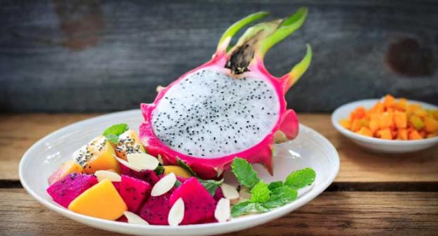 A colorful salad with white dragon fruit, mango, mint, and almonds.